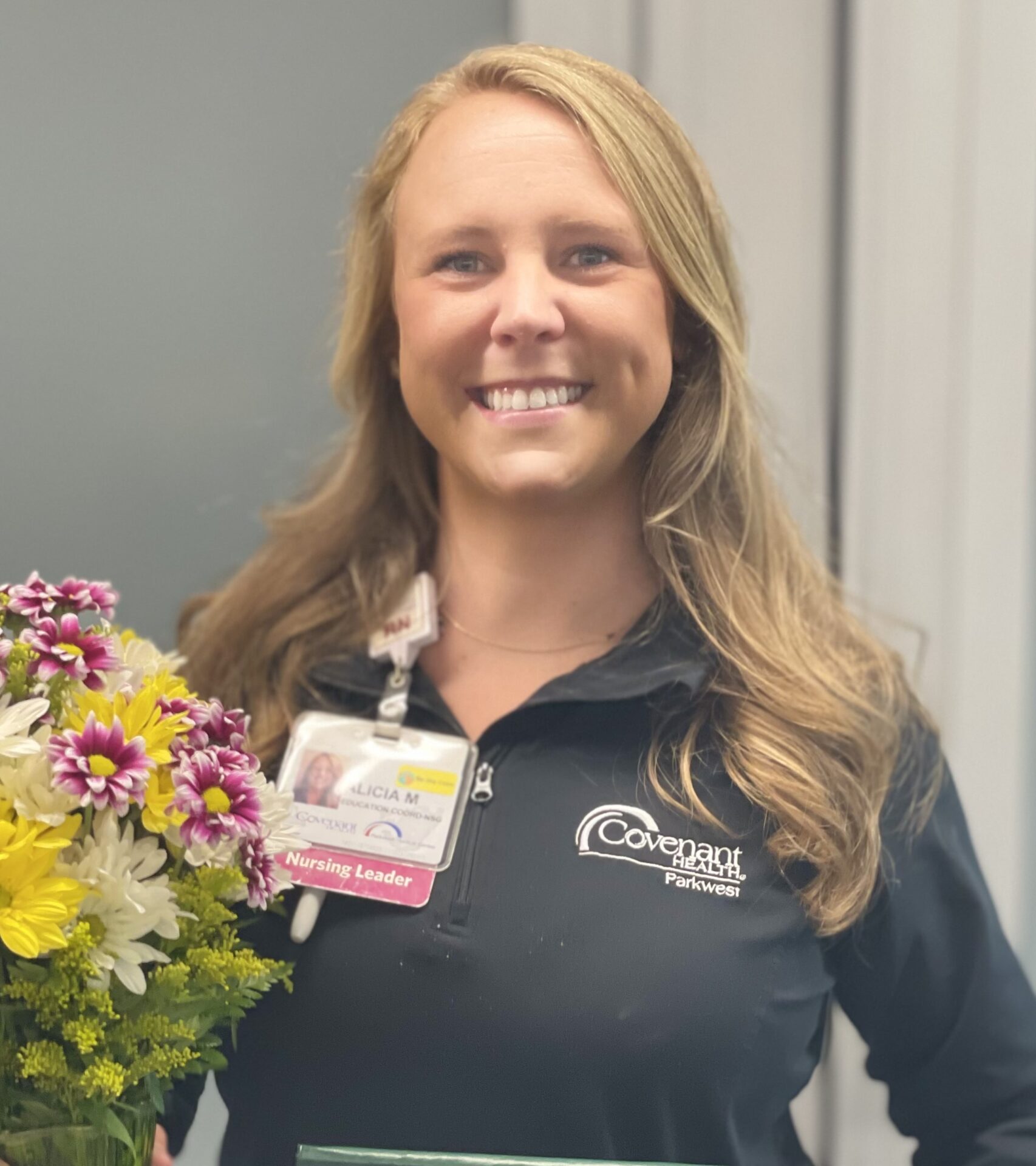 Smiling blonde nurse in black top holding bouquet of daisies.