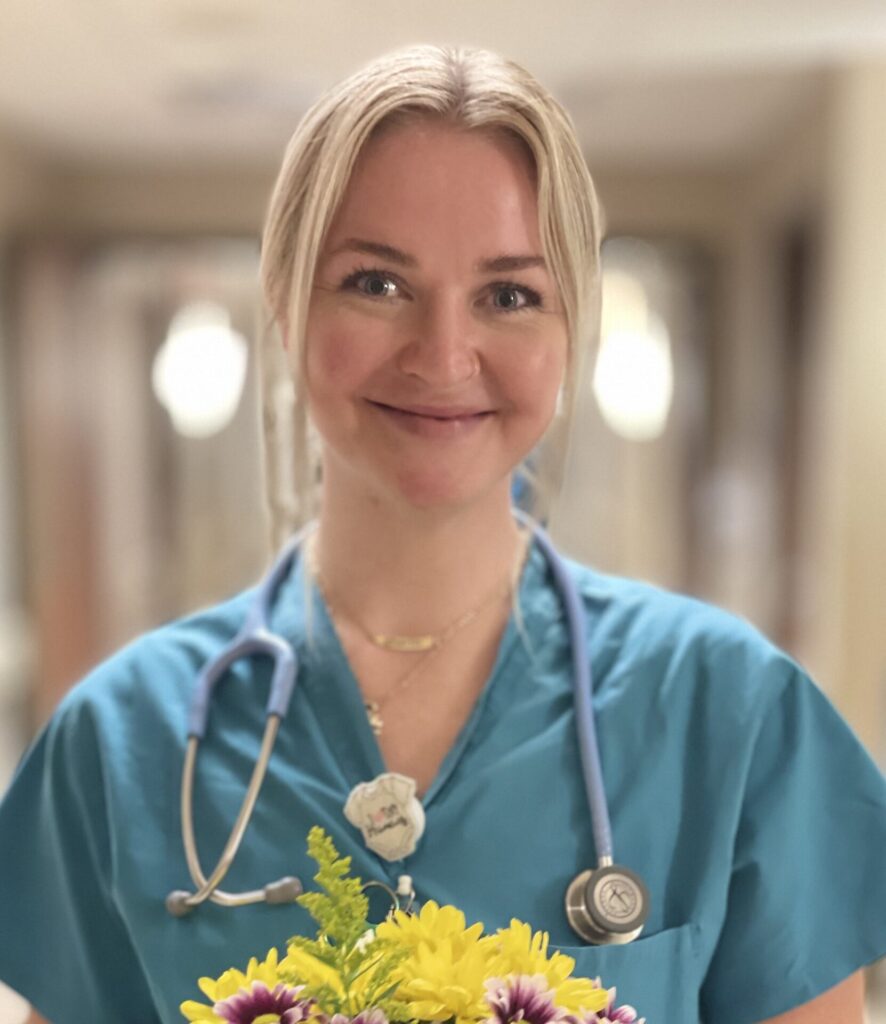 Smiling nurse in green scrubs, holding bouquet of daisies.