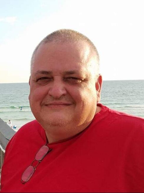 Headshot of James Hamby before bariatric surgery. He is wearing a red t-shirt and has glasses at the neck. Beachfront is visible in the bacground