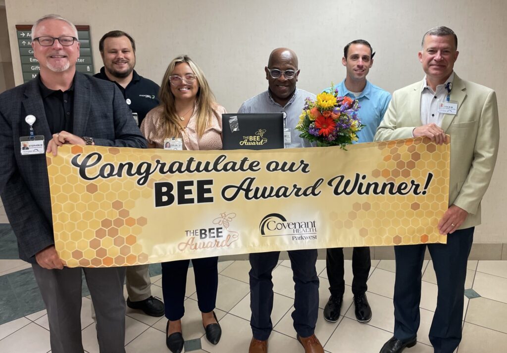 Group of smiling co-workers holding yellow BEE Award banner.