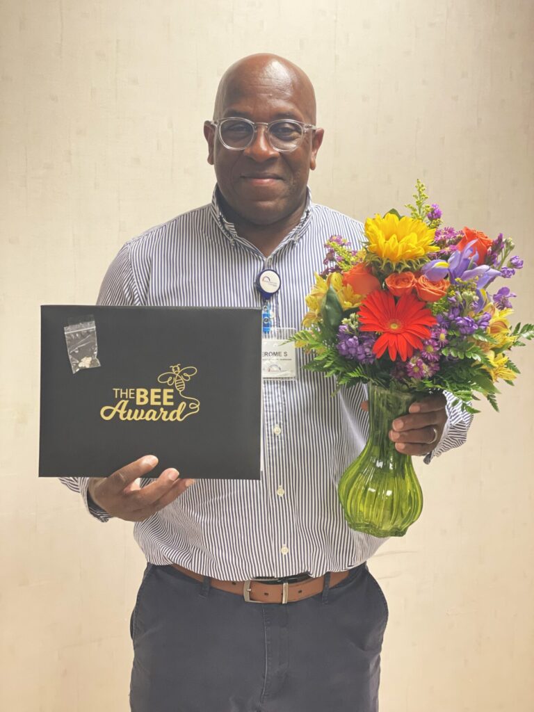 Smiling african american male holding award and flowers.