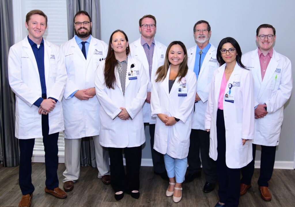 Five men and three women standing together and smiling. All are wearing white coats.