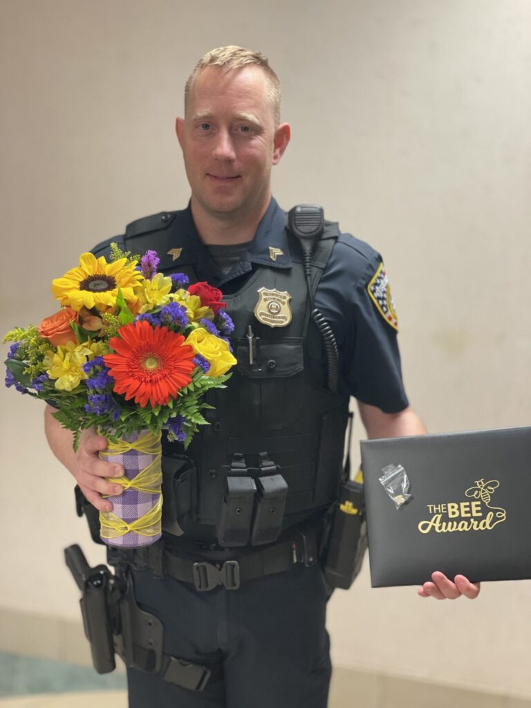 Blonde man with security uniform on holding flowers and BEE Certificate.