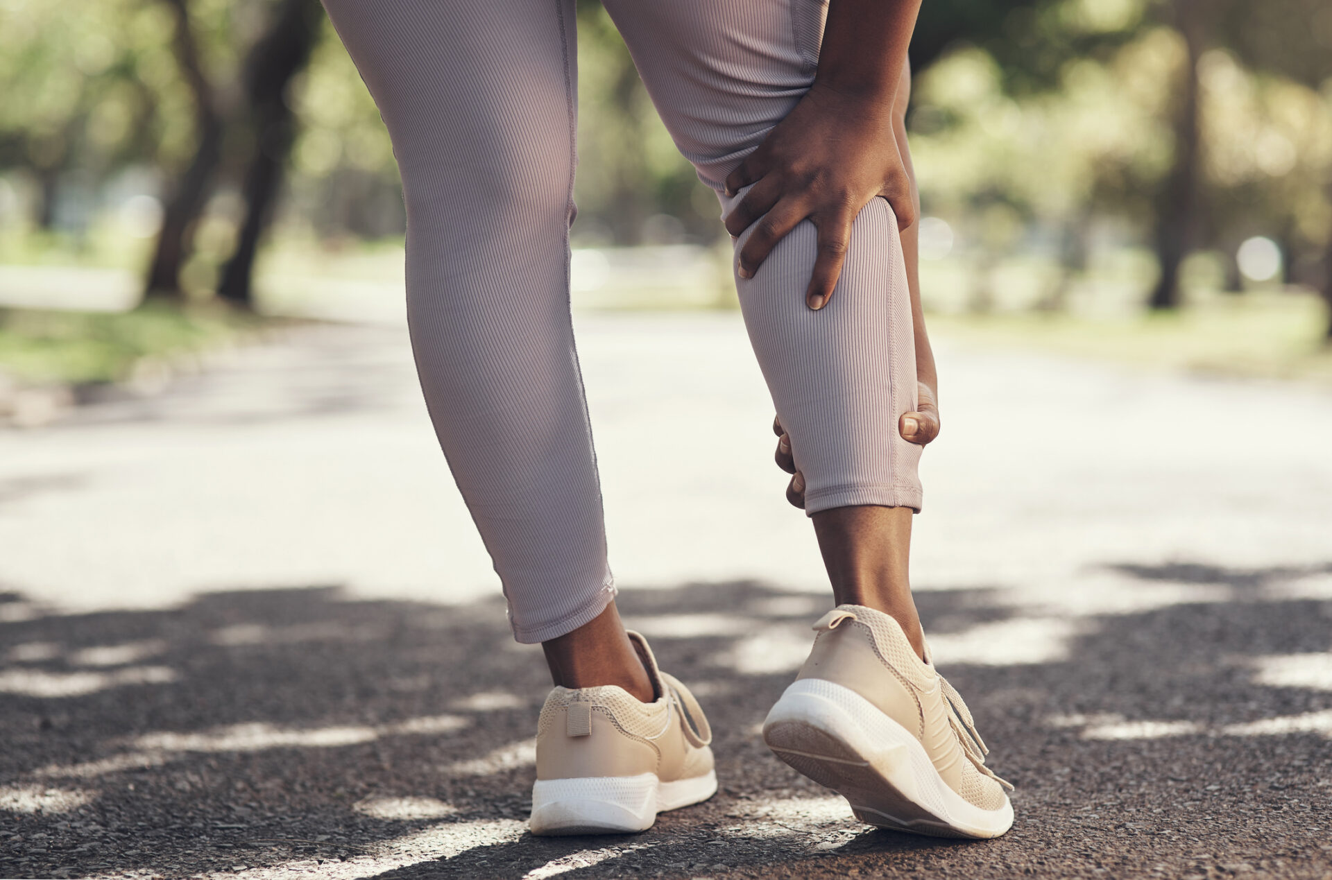 Woman on a path in tennis shoes clutching her calf muscle