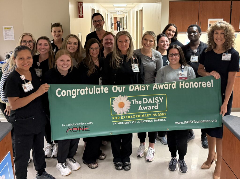 Group of nurses in black scrubs holding green DAISY Award banner.