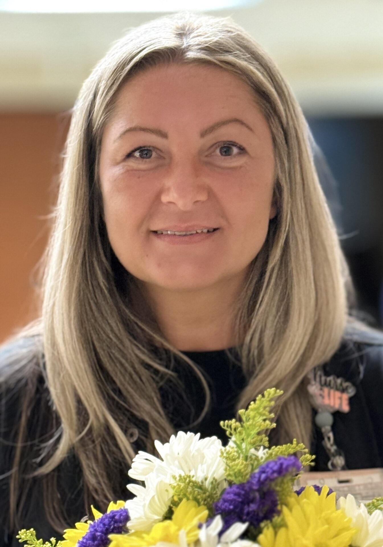 Headshot smiling blond nurse holding daisies.