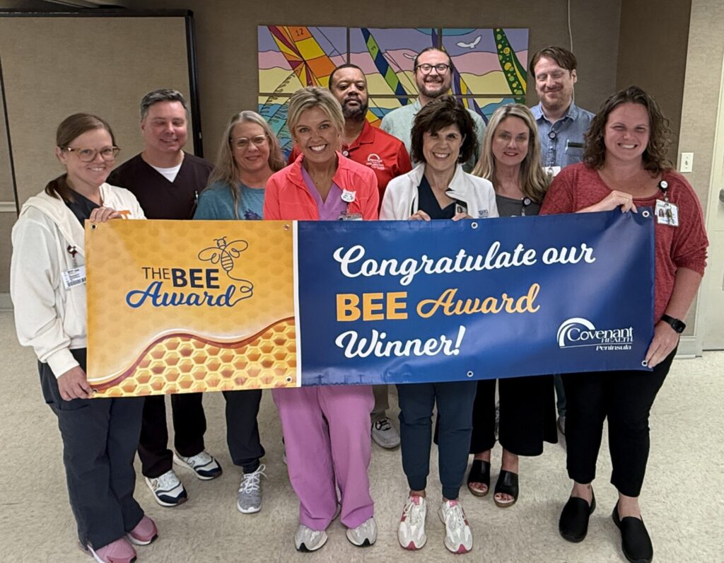 A group of smiling healthcare workers stands indoors holding a banner that reads, Congratulations to our BEE Award Winner! 