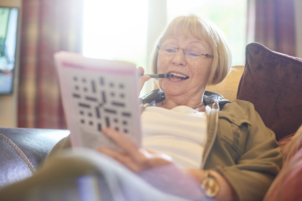 A senior women completing a crossword puzzle while lounging on her couch. 