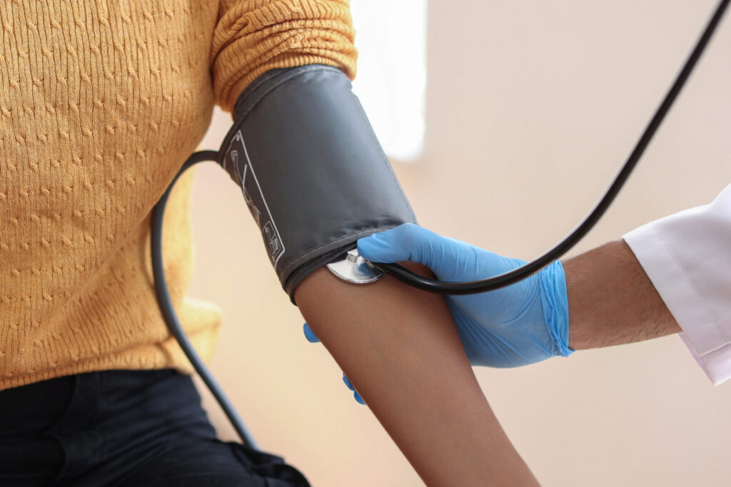 A healthcare professional measures a persons blood pressure using a cuff and stethoscope on the persons upper arm.