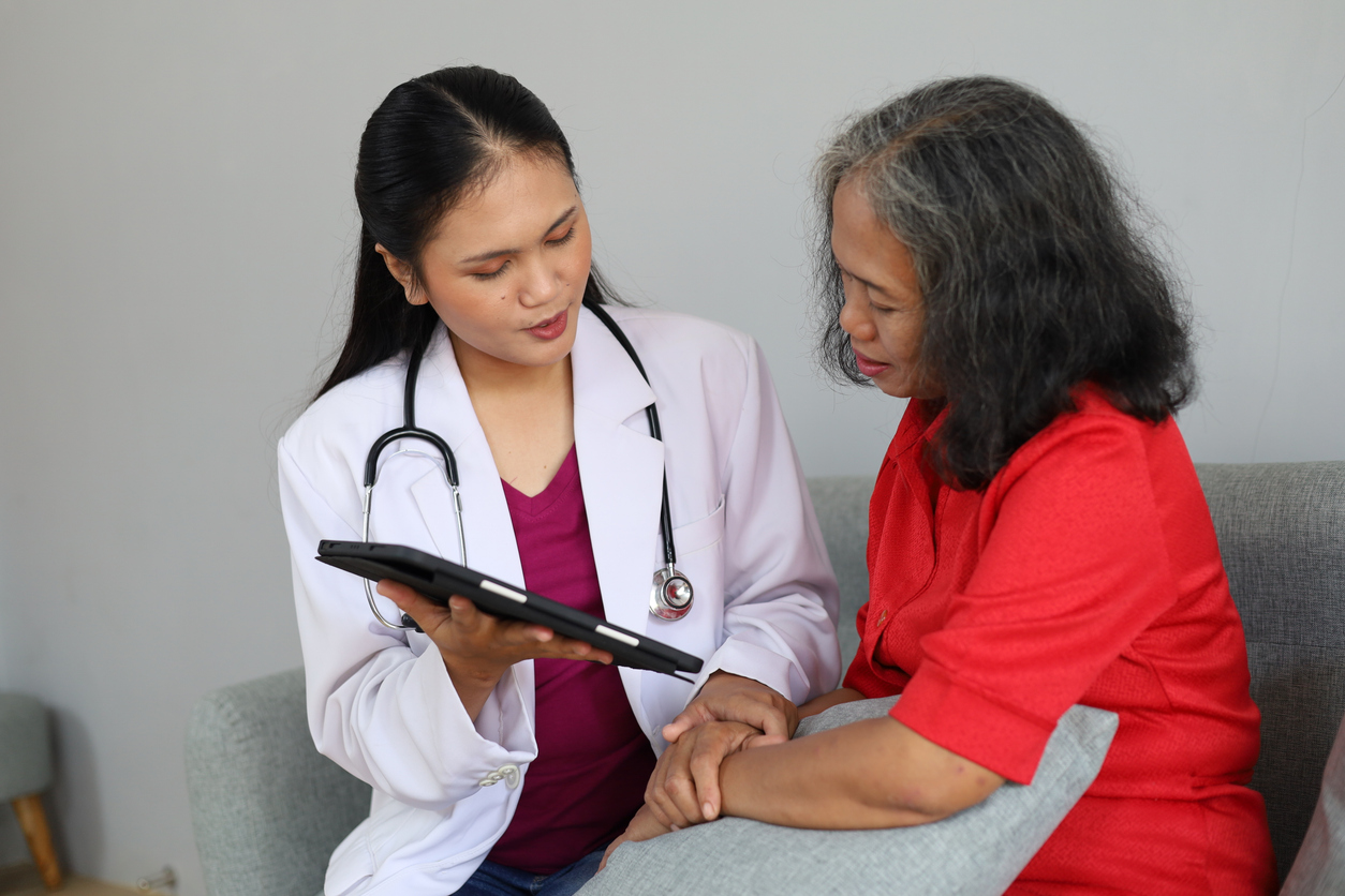 A doctor in a white coat shows information on a tablet to a patient while holding her hand.