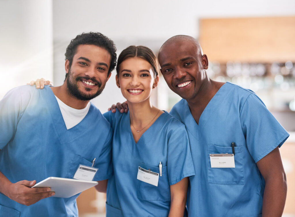 Two adult males and an adult female all in scrubs smiling together.