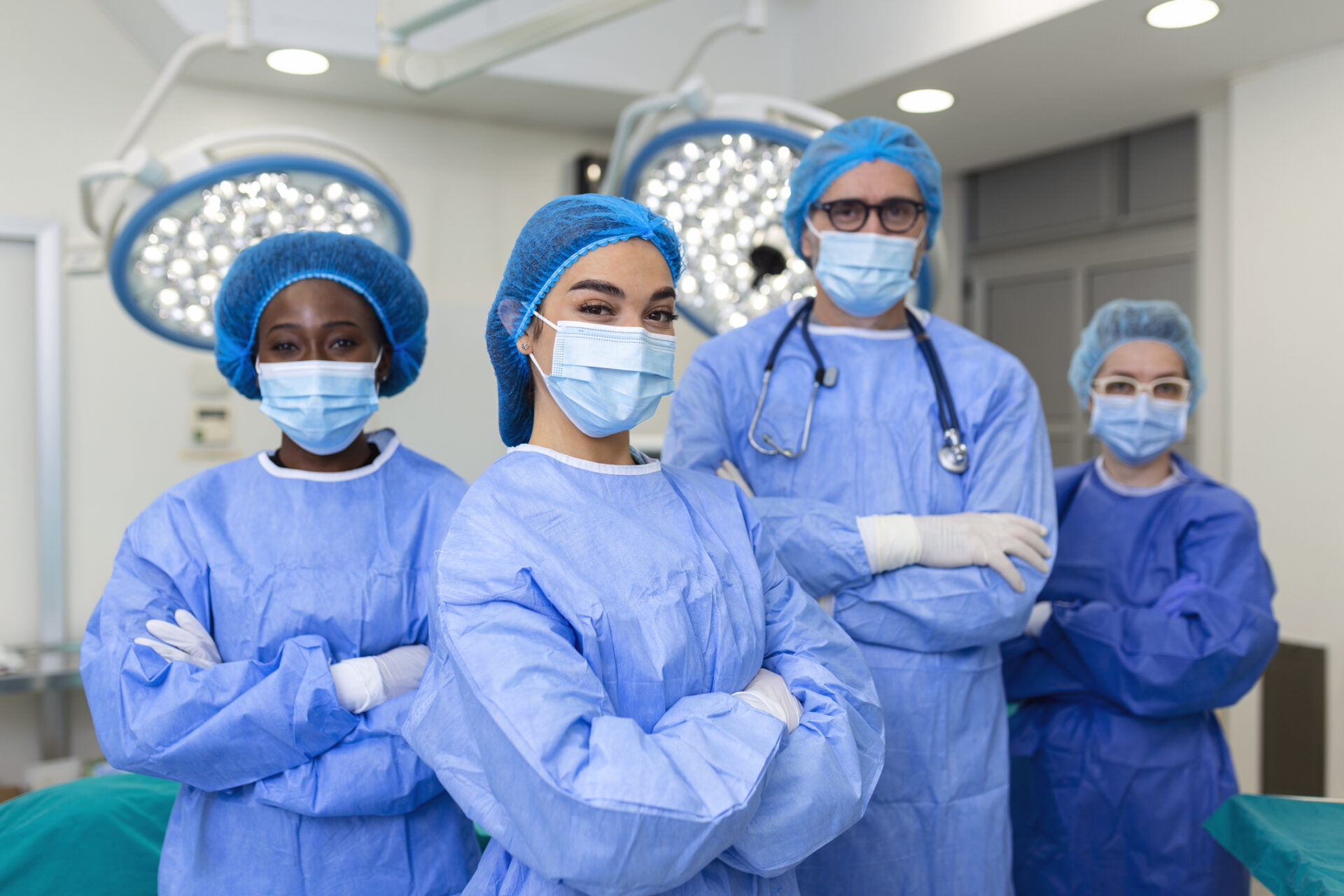 Four surgeons in blue scrubs, surgical masks, and caps stand confidently with arms crossed in a brightly lit operating room—an inspiring scene for those seeking Tennessee CRNA jobs.
