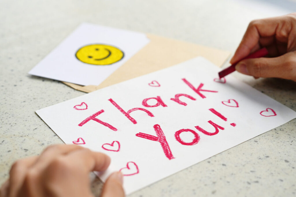 A hand writes Thank You! in red crayon on a card.