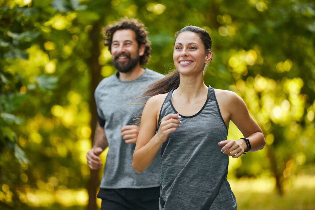 A smiling woman and a man jog together outdoors.