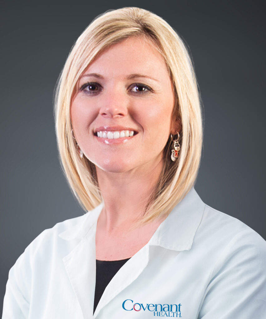 A woman with straight blonde hair wearing a white lab coat and earrings smiles at the camera. The lab coat has the Covenant Health logo on it. The background is a plain dark gray.