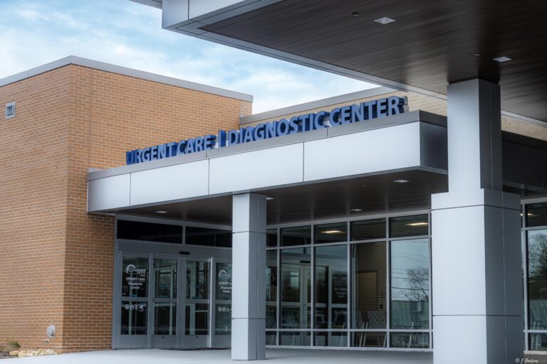 Exterior view of a modern medical building with a sign reading Urgent Care | Diagnostic Center above glass entrance doors, featuring brick and metal architectural elements.