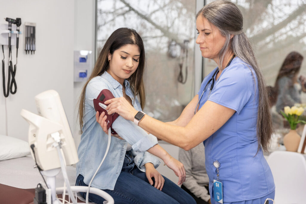 The teenage girl watches as a woman in scrubs puts a blood pressure cuff on her arm. They are in a doctors' office.