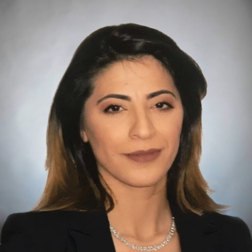 Professional portrait of a woman with shoulder-length dark hair, wearing a black blazer and a silver necklace, against a light gray background. She has a neutral expression, reflecting resilience in managing chronic migraines.