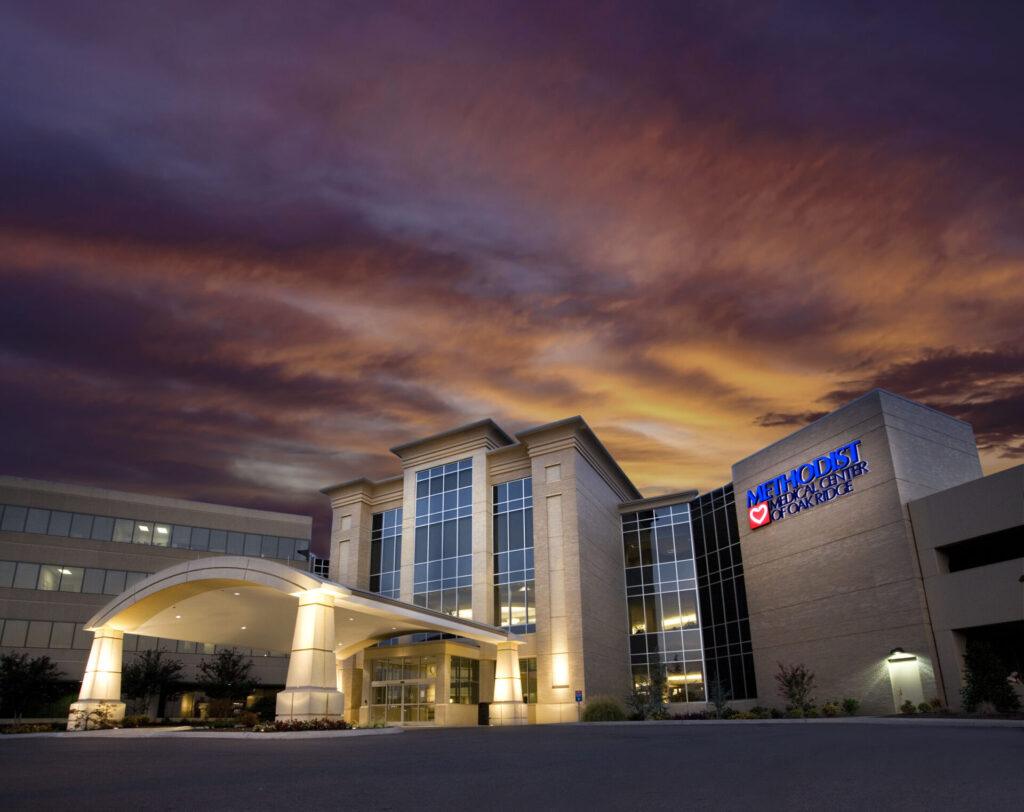 A modern hospital building with bright exterior lights is shown at dusk, under a dramatic, colorful sky. The sign on the building reads Methodist Midlothian Medical Center, part of the trusted Covenant Health Methodist network.