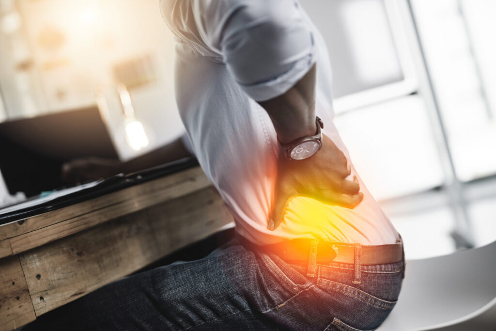 A person sitting at a desk holds their lower back in pain, with a highlighted area indicating discomfort associated with symptoms of shingles.