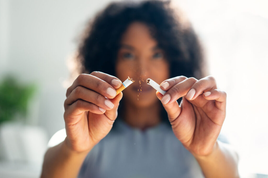 A person with curly hair is holding and breaking a cigarette in half, with tobacco spilling out, symbolizing quitting smoking—a healthy choice that can lower risks faced during procedures like a colonoscopy. The focus is on the hands and the broken cigarette.