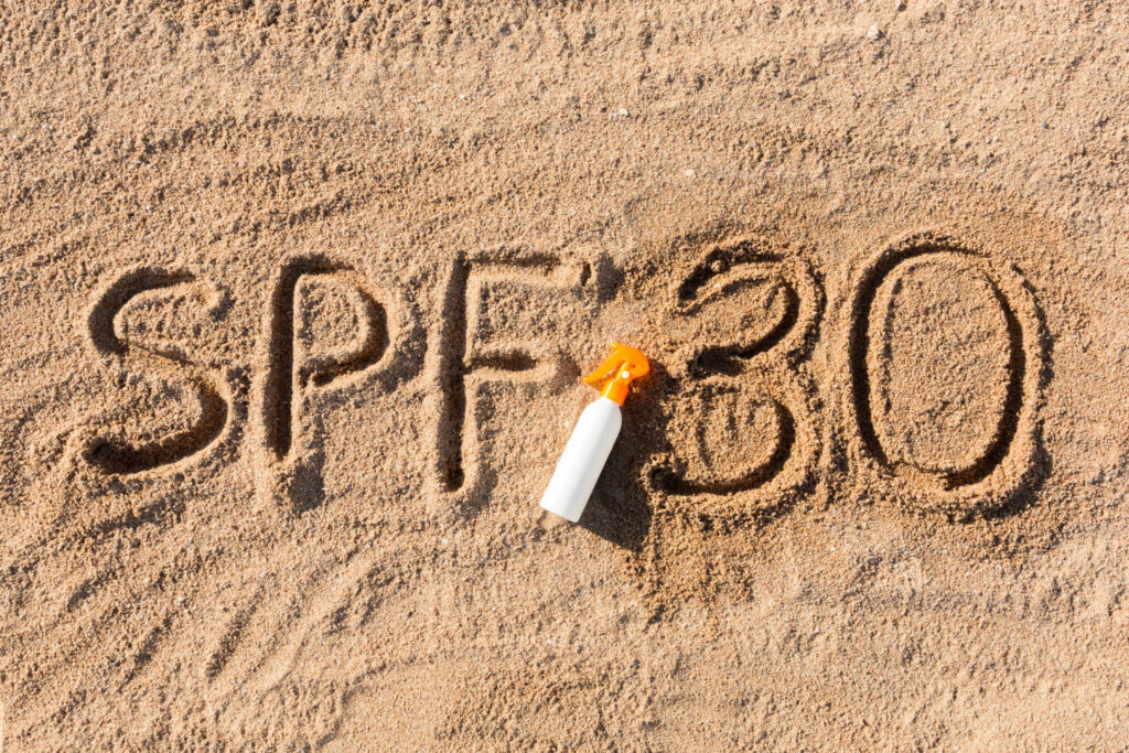 A bottle of sunscreen with an orange cap sits on the sand, where SPF 30 is written—your reminder to follow the 4 Steps to Stay Safe in the Sun and prioritize sun protection.