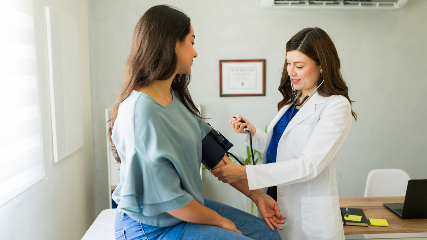 A doctor in a white coat checks a patient’s blood pressure in a medical office at the Metabolic Clinic Oak Ridge. The patient sits on an exam table while the doctor uses a stethoscope and blood pressure cuff.