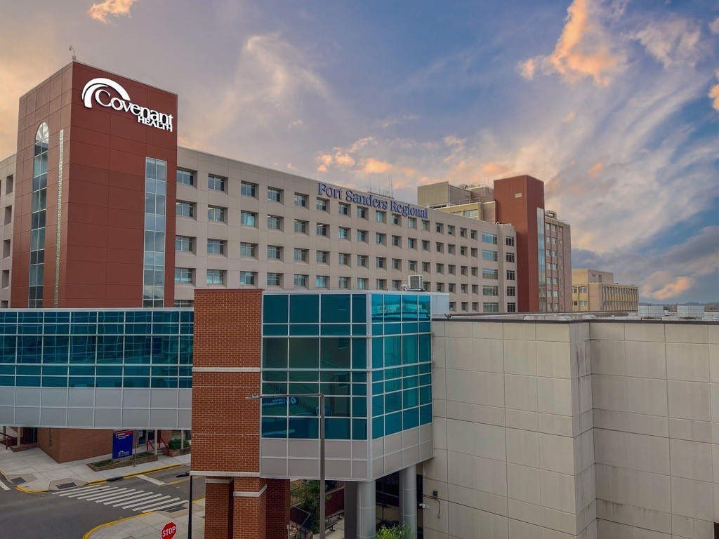 Fort Sanders Regional Medical Center building with Covenant Health sign, glass skywalk, and blue sky with clouds at sunset.