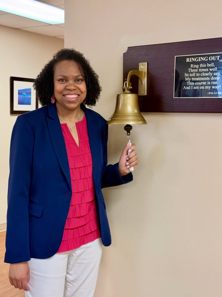 After completing breast cancer treatment, Stacey Bussell returns to the cancer center and stands beside the ringing bell, reflecting on the support she received from her care team.