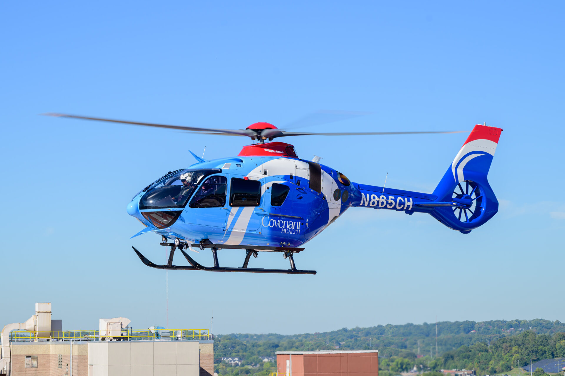 A blue Covenant Health emergency medical services helicopter in flight over a building.