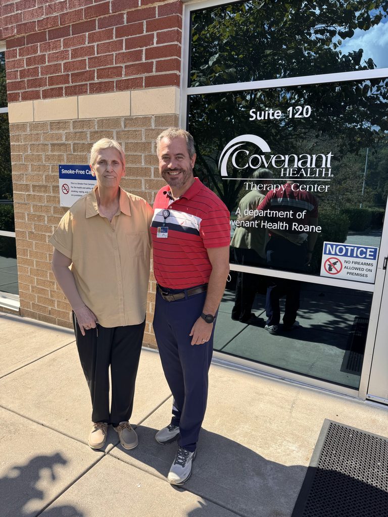 A woman and a man stand smiling together outside the entrance to a Covenant Health Therapy Center.