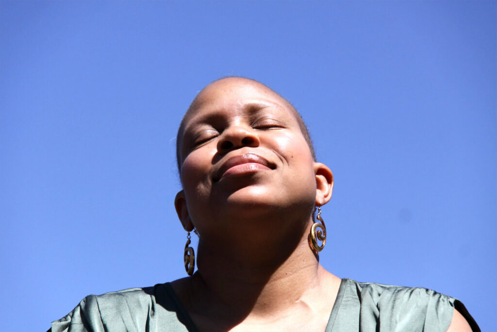 A person with their head tilted back and eyes closed against a clear blue sky.